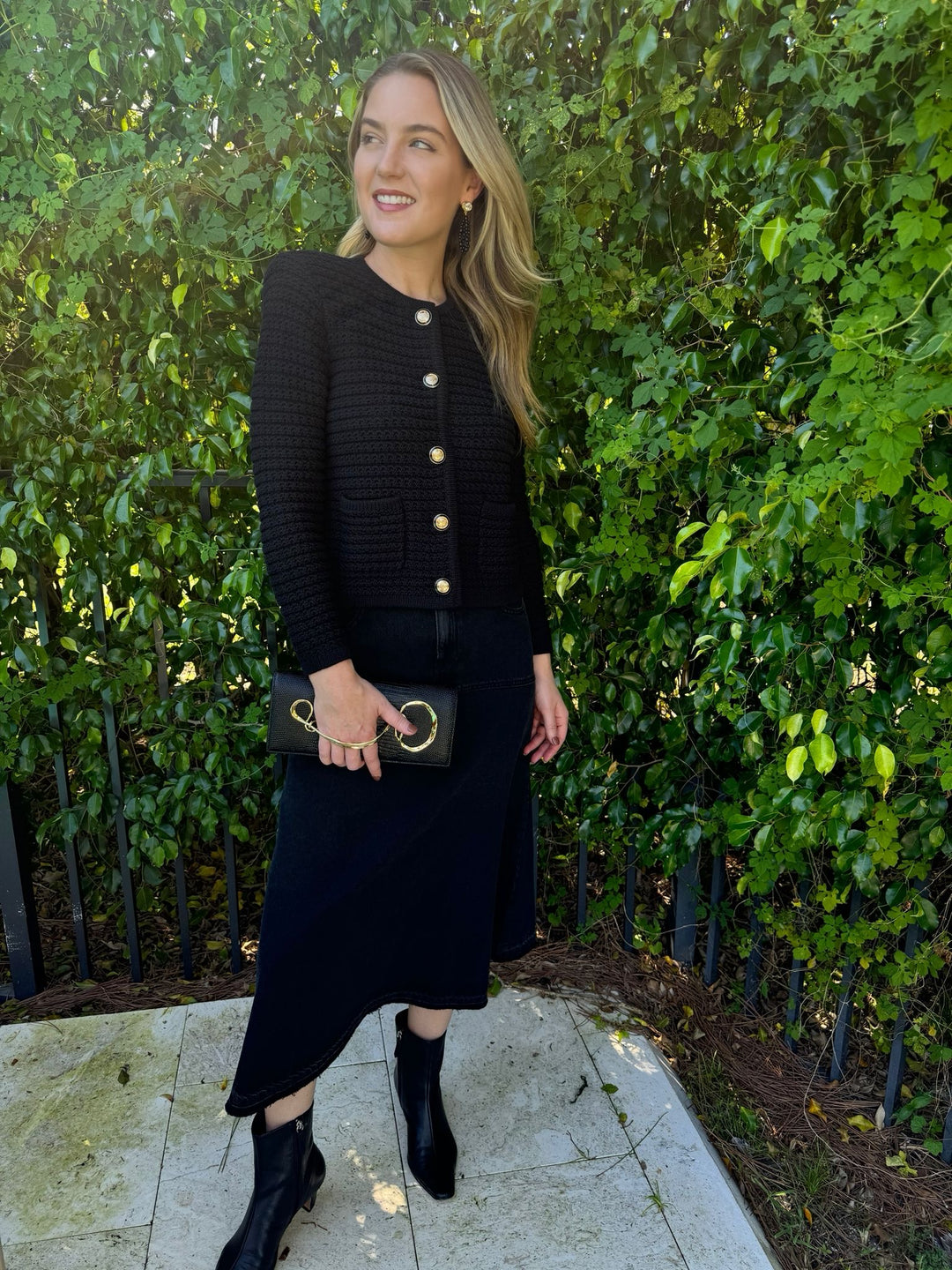 Ba&sh Volentia Denim Midi Skirt in Blackstone paired with Gaspard Knit Cardigan in Noir, Lizzie Fortunato Midnight Masquerade Earrings, Alexis Bittar Twisted Gold Side Handle Clutch Bag in Black available at Barbara Katz