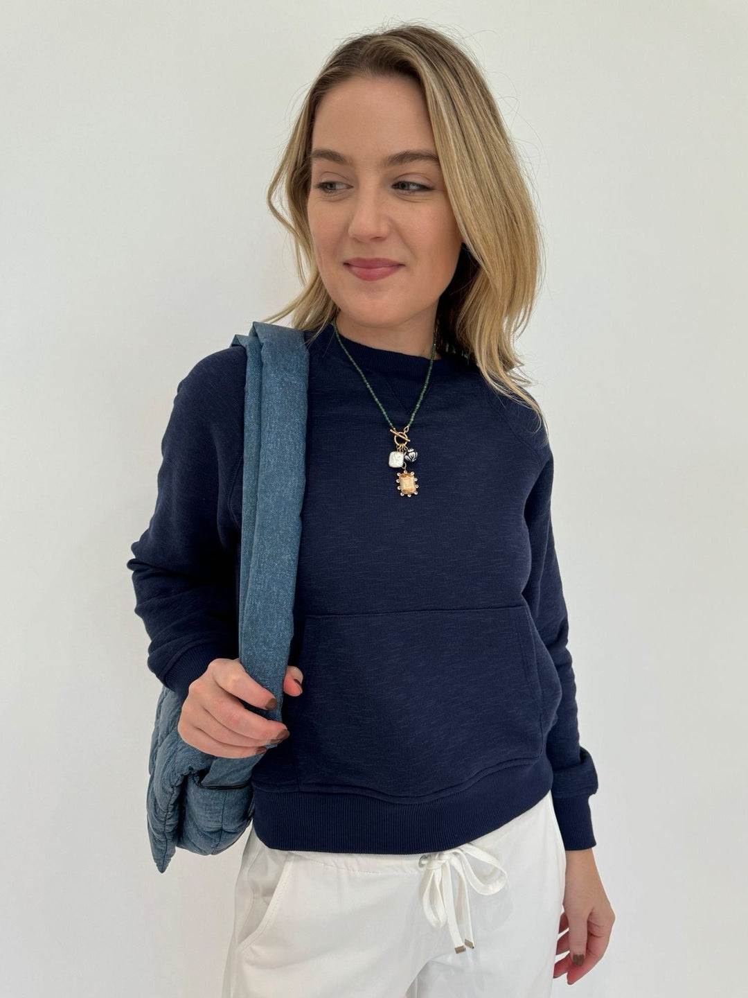 BK Fiona Crew Neck Sweatshirt in Dark Night paired with Raffaello Rossi Candice Straight Pants in White, Mignonne Gavigan Delancey Charm Necklace, Vee Collective Porter Messenger Bag in Denim - all available at Barbara Katz