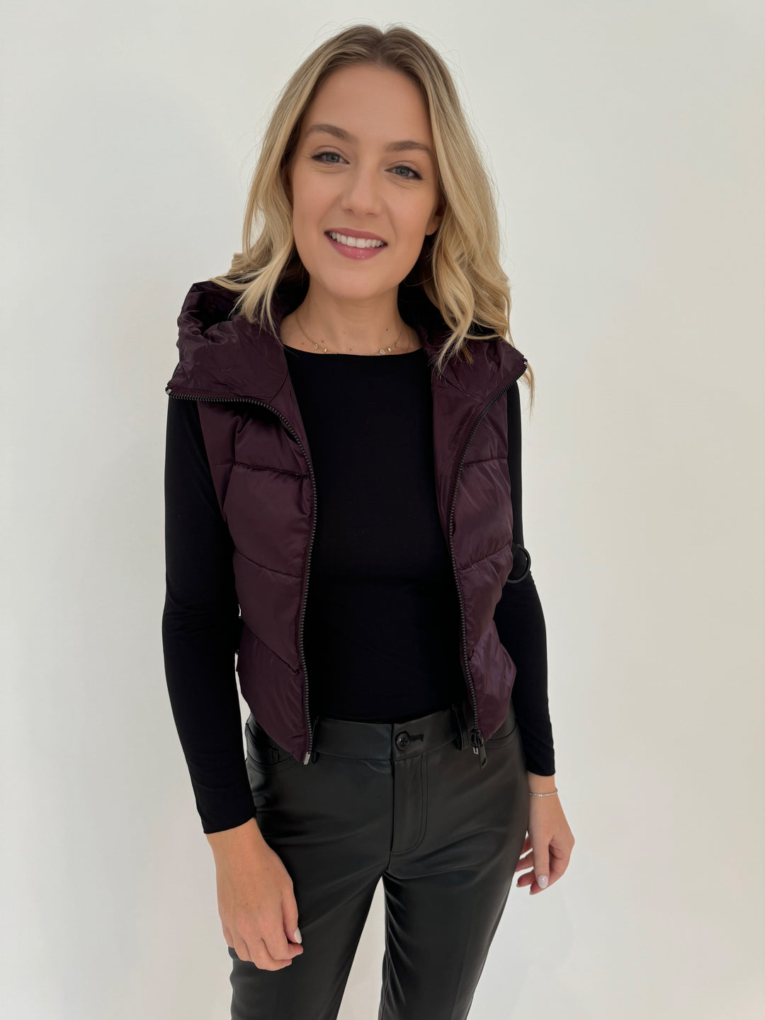 Adroit Atelier Lola Quilted Full Zip Vest in Burgundy with AMB Black Solid Raw Edge High Neck Second Skin Top underneath, paired with Peace of Cloth Black Faux Leather Slim Jeans, all available at Barbara Katz