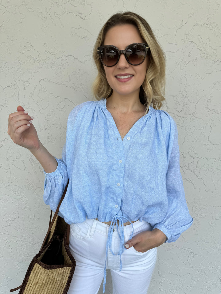 Kerri Rosenthal Honey Jayney Blouse in Windsurfer, light blue top made from 100% linen featuring smocked neckline, shell button front, bubble blouson sleeves, embroidered heart on sleeve, and interior drawcord at waist