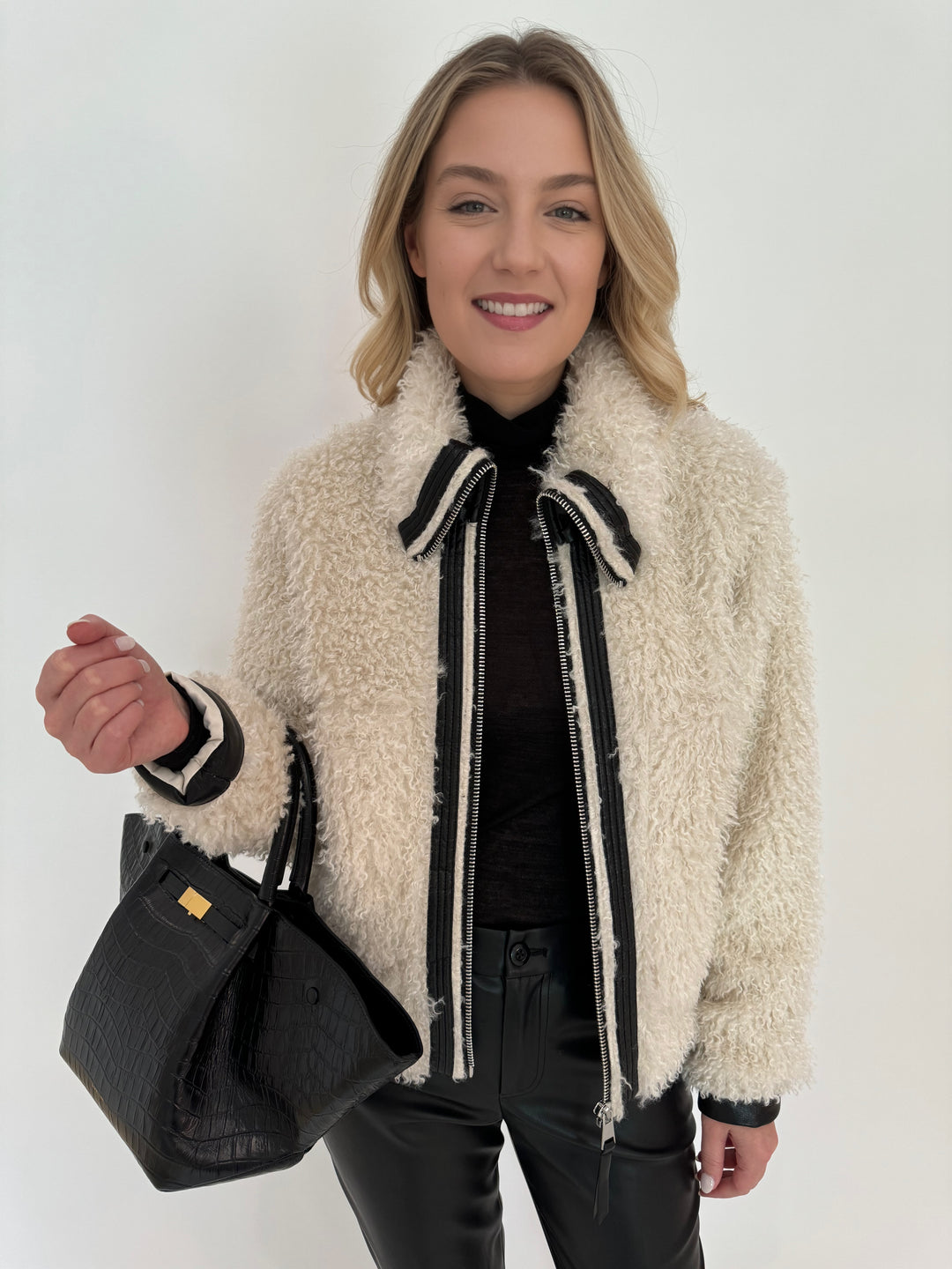 Adroit Atelier Carrie Short Mongolian Faux Fur Coat in Ivory paired with Peace of Cloth Black Faux Leather Slim Jeans, bag DeMellier The New York Tote in Black Croc Effect, all available at Barbara Katz